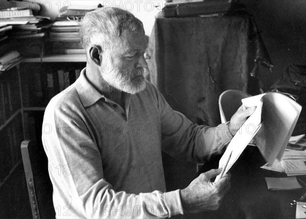 Author Ernest Hemingway sitting at a desk reading