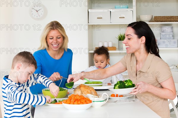 Same sex female couple having dinner with their sons in their home.