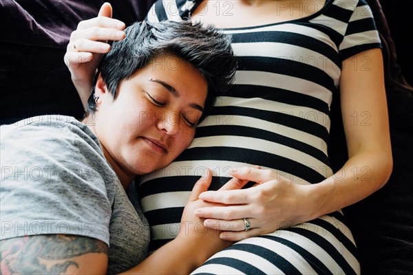 Pregnant lesbian couple cuddling on sofa