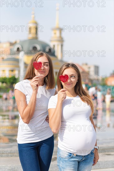 Lesbians mothers, pregnant couple, happy samesex family in the city park at summer. Women holding sweets, heart shaped candies, symbol of love.