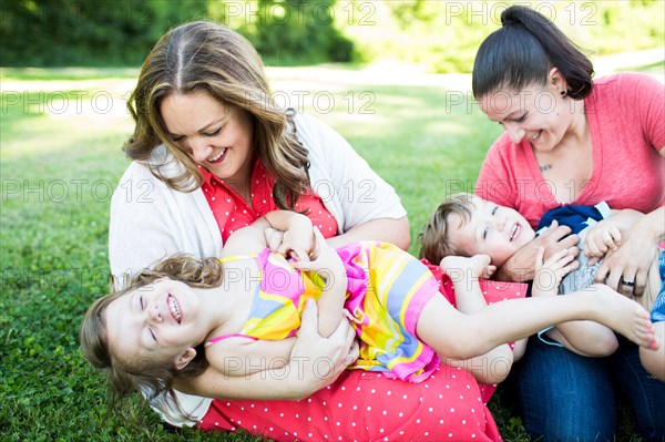 Playful lesbian mothers playing, tickling children in grass