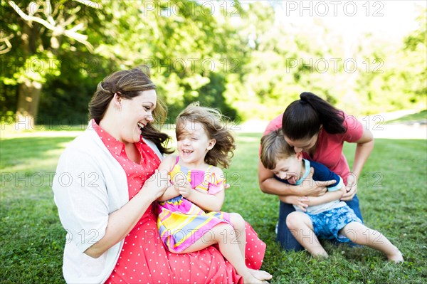 Lesbian mothers playing, tickling children in summer grass yard