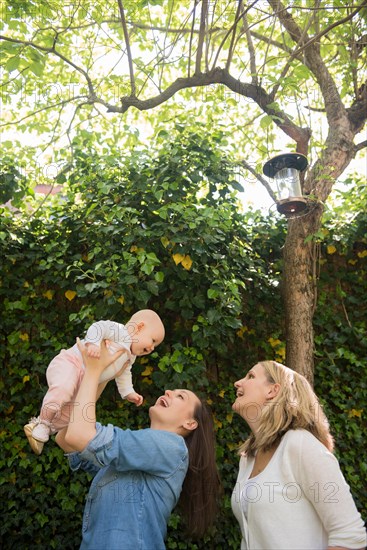 Caucasian mothers lifting baby daughter under tree