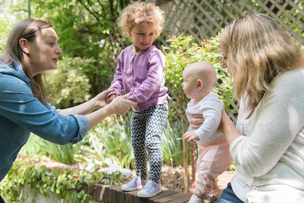 Caucasian mothers holding daughters on garden wall