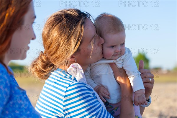 Loving mother embracing her baby and  sitting on wooden bench at tropical beach during vacation. They together looking into the distance. Concept for