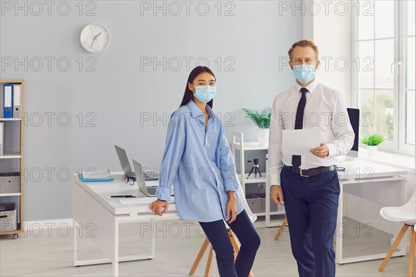 Business colleagues in medical protective mask with documents looking at camera in office