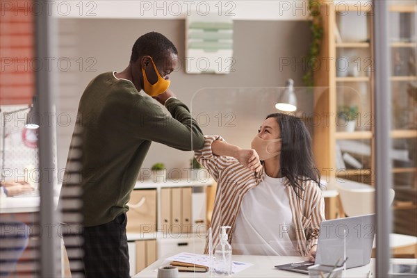 Portrait of two colleagues touching elbows as contactless greeting in office while wearing masks