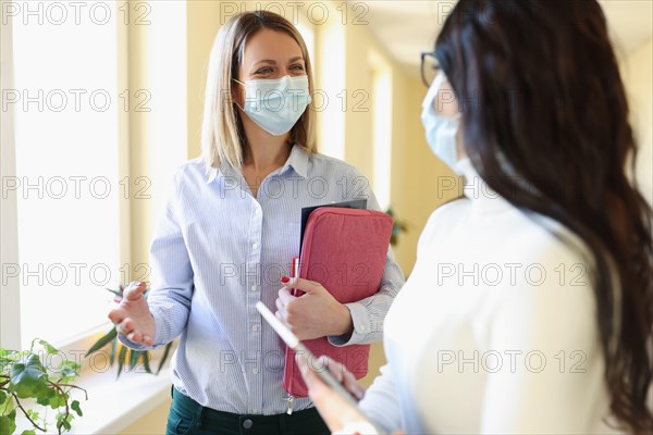 Two businesswoman in medical protective masks are talking in office.
