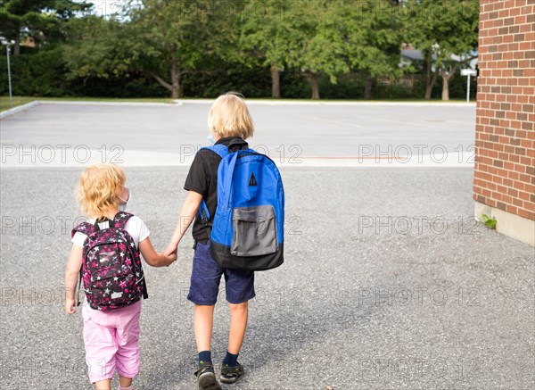 Children in masks going to school and kindergarten, holding hand, wearing backpacks. Children near school wearing masks during virus outbreak. Back to