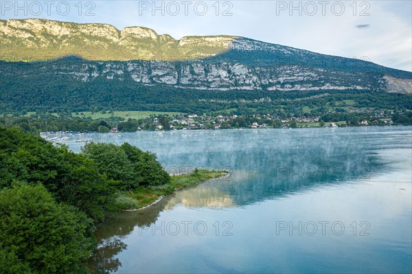 Small town below a mountain near a lake covered in fog in France