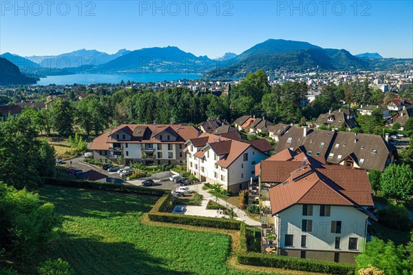 Complex of houses with mountains and large lake in distance. Aerial view of residential real estate in Annecy, France