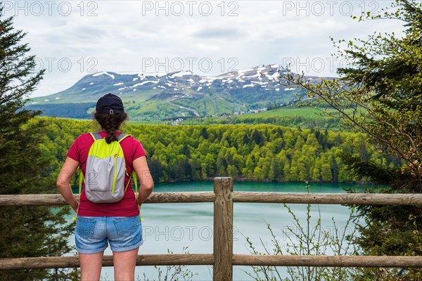 Young woman (unrecognizable back view) admiring view of lake Pavin in Auvergne Volcanic Regional Nature Park, France.  Active holidays in nature backg