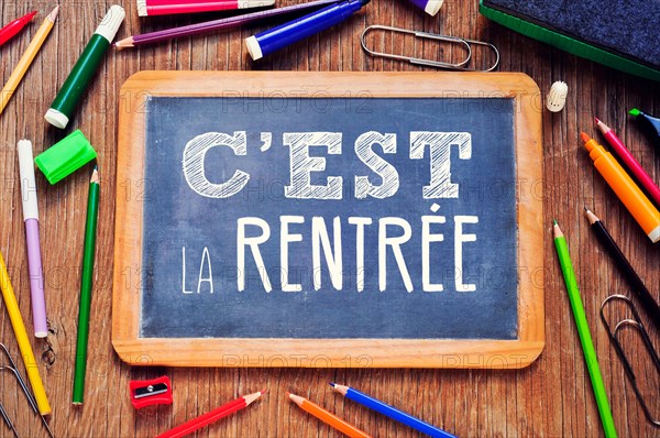 high-angle of a chalkboard with the text cest la rentree, back to school written in french, on a rustic wooden table full of mar