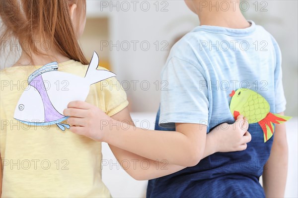 Little children sticking paper fish on each other indoors. April fool's day prank