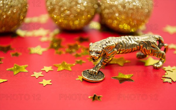 A bronze figure of a tiger with a coin - the symbol of the Chinese new year 2022 on a background of red, gold stars and balls, a copy space.