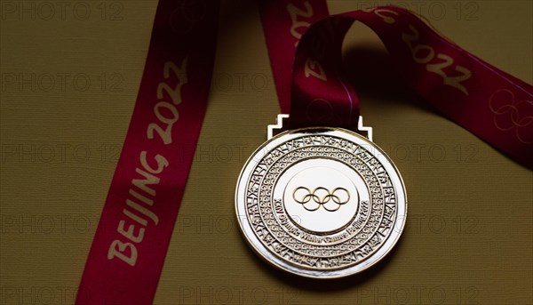 January 14, 2022, Beijing, China. Gold medal of the XXIV Olympic Winter Games on a yellow background.
