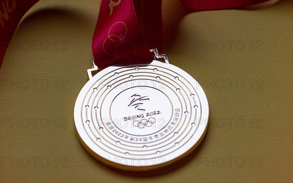 January 14, 2022, Beijing, China. Gold medal of the XXIV Olympic Winter Games on a yellow background.