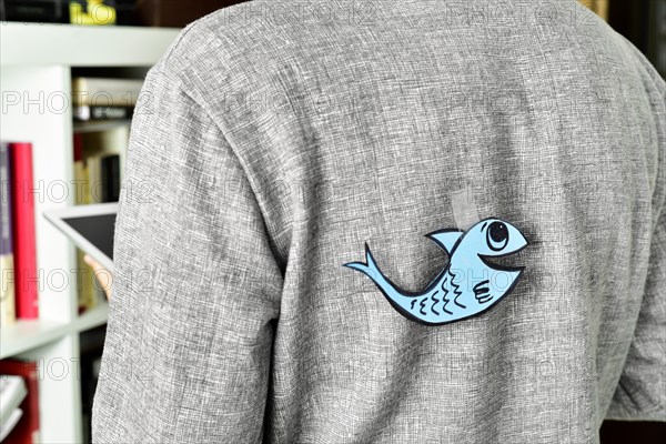 closeup of a young man with a paper fish attached with tape to his back