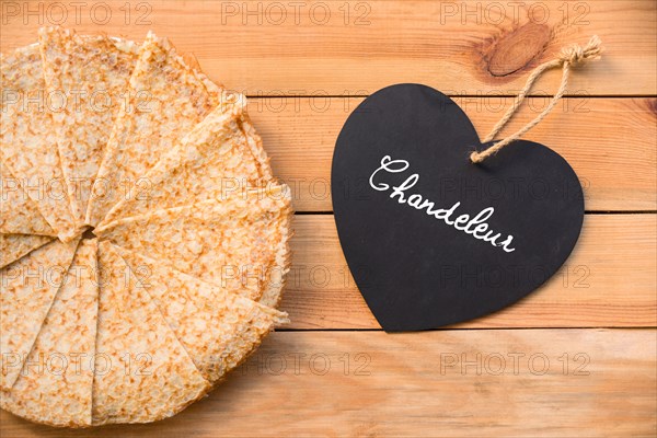 Top view of crepes (french pancakes), word chandeleur (meaning candlemas) written on a heart, rustic wood background