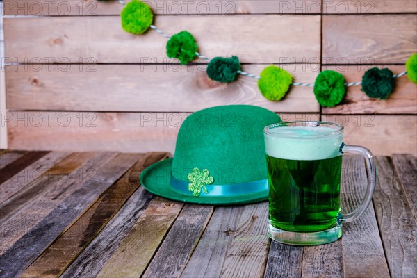 Mug of green beer with Irish festive hat on wooden background. Tabletop, front view.