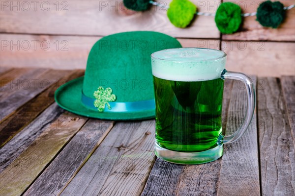 Mug of green beer with Irish festive hat on wooden background. Tabletop, front view.