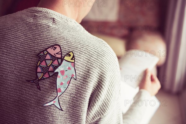 young caucasian man seen from behind with two paper fishes attached to his back, as a popular prank for april fools day in countries such as Italy, Fr