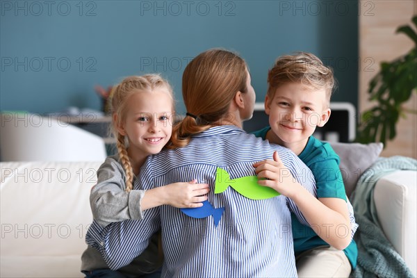 Little children sticking paper fish to their mother's back. April fools' day prank