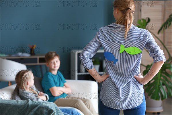 Mother with paper fish on her back scolding children. April fools' day prank