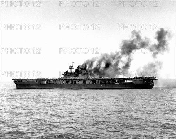 USS Yorktown (CV-5) dead in the water after being hit by Japanese bombs on 4 June 1942. The ship was hit shortly after noon. This view was taken about an hour later, with fires still burning in her uptakes but other immediate repairs well advanced. F4F-4 fighters that had been parked at the forward end of the flight deck during the attack have been respotted aft, in take off position. Two SBD-3 scout bombers can be seen through the open sides of her after hangar bay.