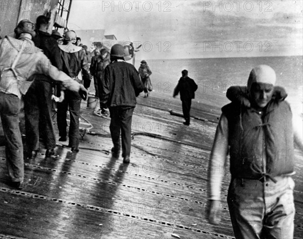 Scene on the flight deck of USS Yorktown (CV-5) shortly after she was hit by two Japanese aerial torpedoes, 4 June 1942. Men are balancing themselves on the listing deck as they prepare to abandon ship. This view looks aft from alongside the island. F4F-4 Wildcat fighter visible in the background is Fighting Squadron Three's Plane # 6, which had been flown by Ensign Brainard T. Macomber during the morning attacks on the Japanese carrier fleet. Insufficient fuel prevented it from being launched to defend Yorktown from the afternoon torpedo plane attack. Note life jacket worn by