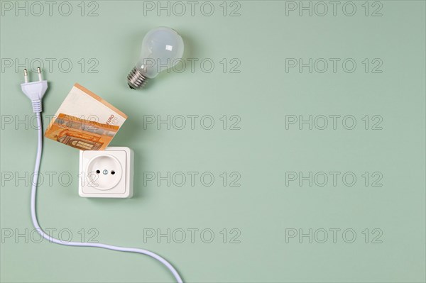 Electric power plug, light bulb and electric socket with Euro banknotes on light green background. Electricity cost and expensive energy concept