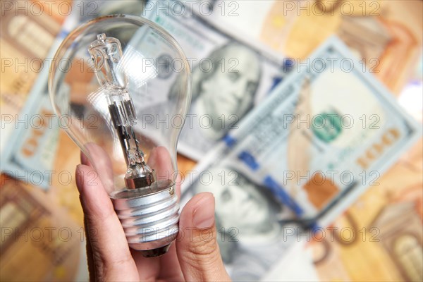 Female hand holding a light bulb on a background of banknotes. Concepts of energy efficiency, electricity expensive cost and power consumption.