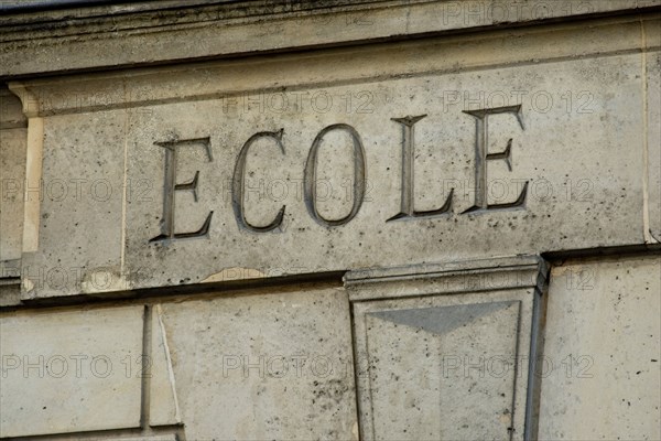 The word ECOLE engraved in stone on the facade of an old building in France