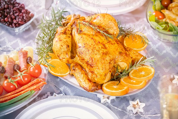 Christmas dinner. Closeup photo of tasty baked chicken against glowing Christmas lights and burning candles. Holiday decorated table, Christmas tree,