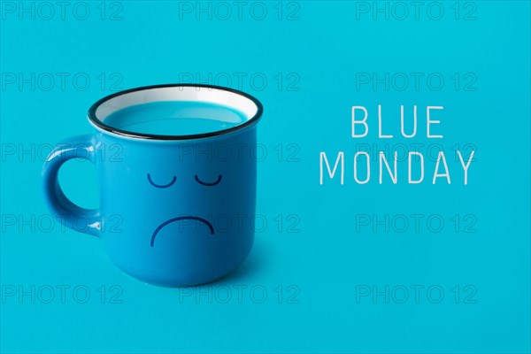 closeup of a blue mug, with a sad face drawn in it, and the text blue monday on a blue background