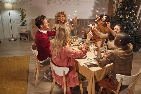 Wide angle view of people toasting with champagne glasses while enjoying dinner party at Christmas with friends and family and holding sparklers, copy space