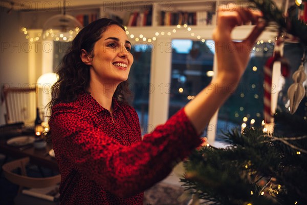 Woman decorating Christmas tree at home. Female hanging decorative items on Christmas tree indoors.