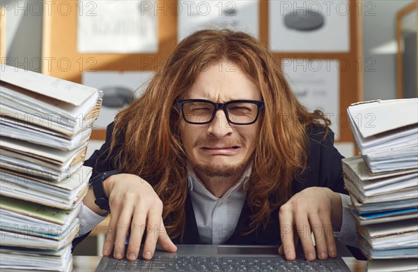 Funny unhappy office worker sitting at desk and crying stressed by huge workload