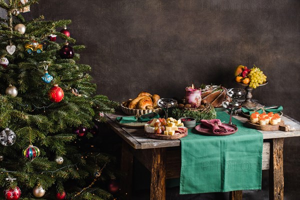 Stylish table setting for christmas family dinner with christmas tree on the background and gifts on the chair.