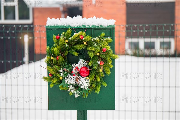 Domestic mail box decorated with spruce tree Christmas wreath outdoors in snowy winter day. Holiday moods.