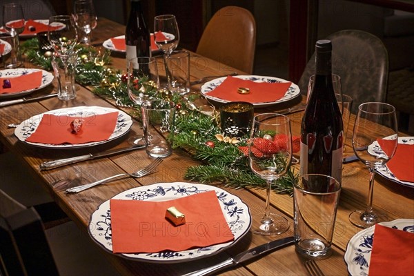 Large rustic wooden table festive set and decorated for a dinner with friends or family, white patterned plates, red napkins, wine and glasses, select