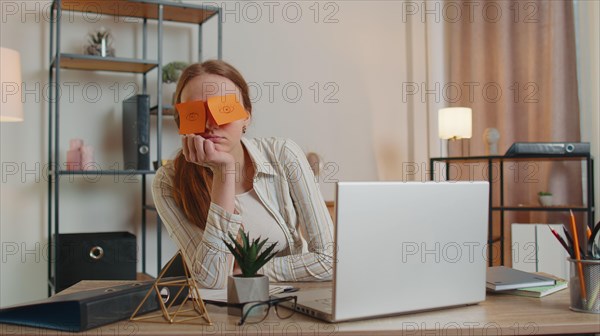 Tired woman teacher using laptop computer with funny stickers on eyes sleeps at workplace, napping