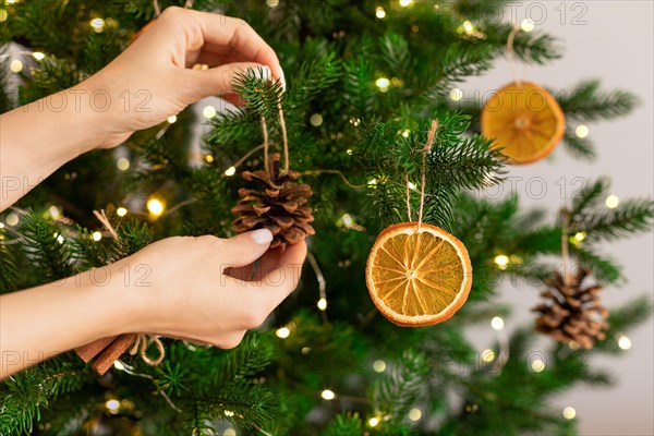 Female hands hanging handmade decoration on Christmas tree.