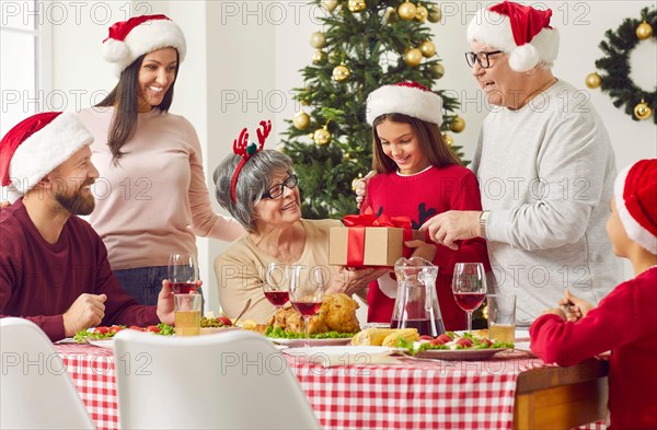 Grandparents giving Xmas gift to granddaughter during family Christmas Thanksgiving dinner.