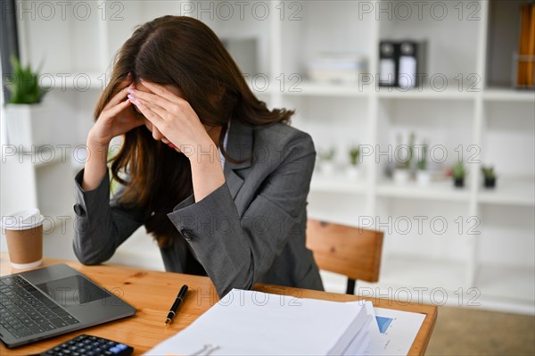 Stressed and sad young Asian businesswoman or female office worker sitting at her desk, suffering from headache, mental health unstable, depressed, ti