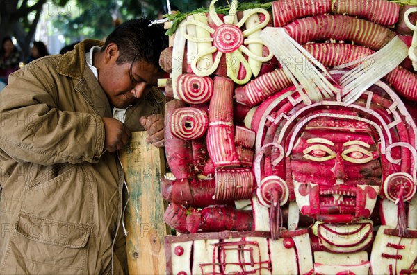 Young man carving Mixtec God of Death mask sculpture at Noche de Rabanos / Night of the Radishes festival, Oaxaca, Mexico.