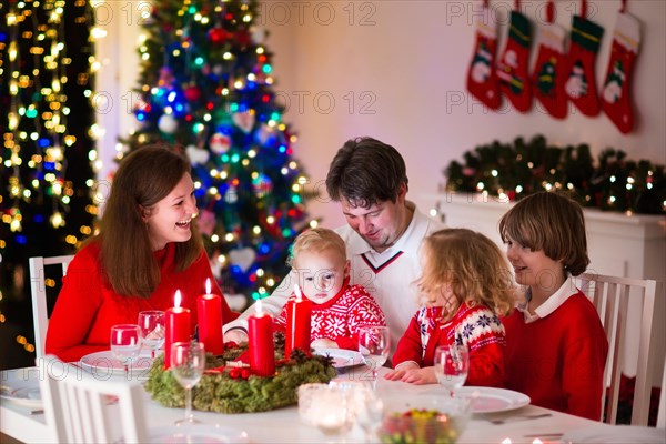 Big family with three children celebrating Christmas at home. Festive dinner at fireplace and Xmas tree. Parent and kids eating