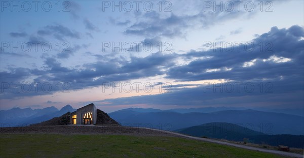 Distant view towards illuminated entrance at dusk. Messner Mountain Museum Corones, Mount Kronplatz, Italy. Architect: Zaha Hadi