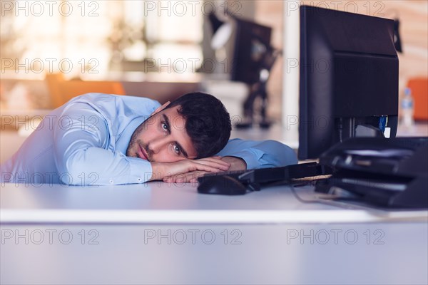 Portrait of a depressed office worker laying on his desk and thinking