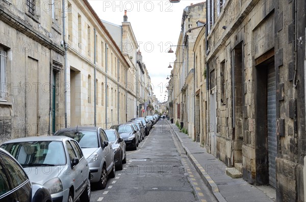 Many modern cars are parked at the side of the ancient narrow straight street in the French city Bordeaux.